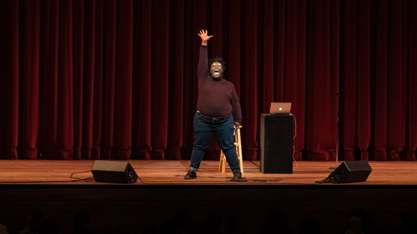 Comedian raising arm and opening mouth on stage 